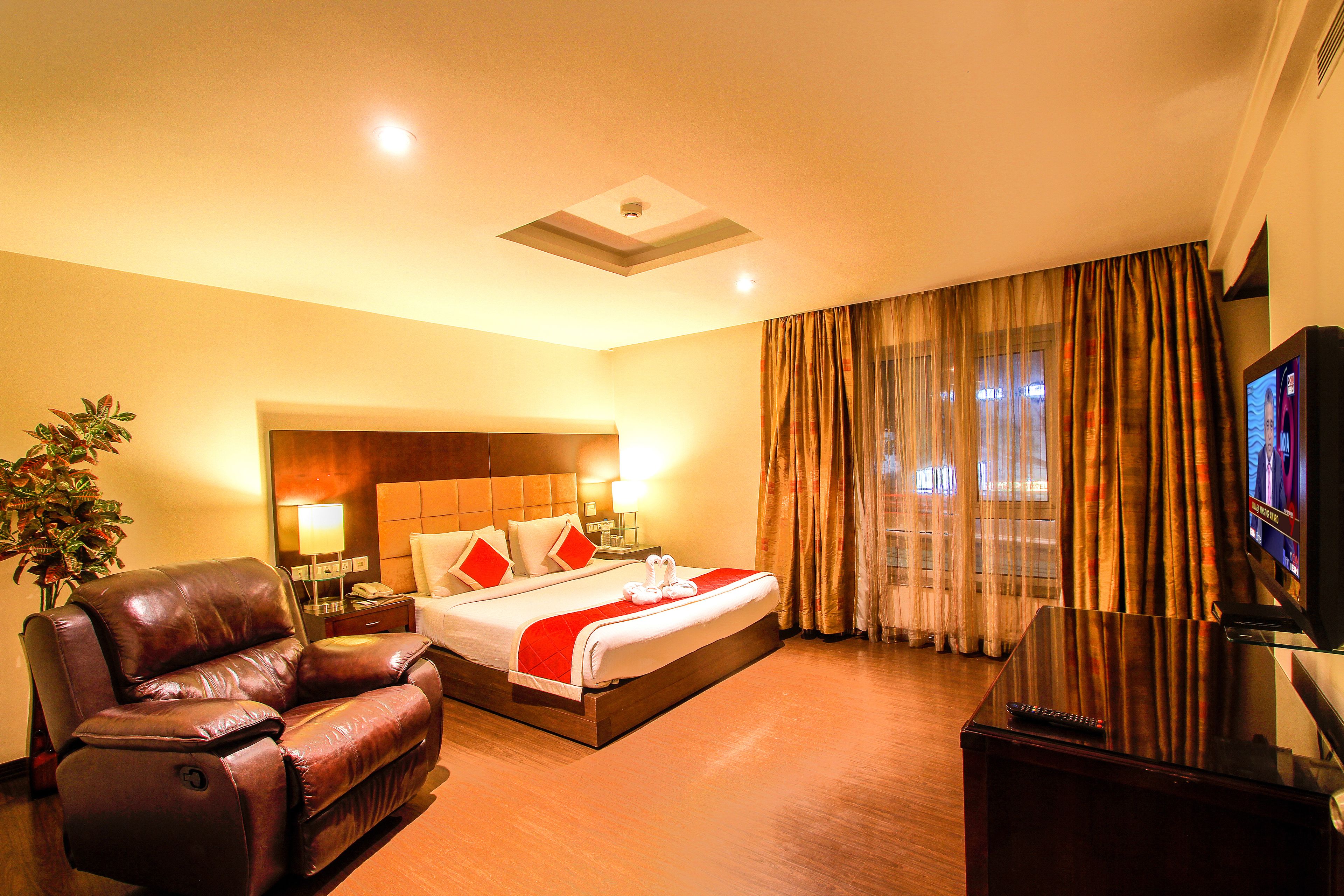 A hotel room with a bed, a leather sofa, a TV, and a nightstand with a lamp.