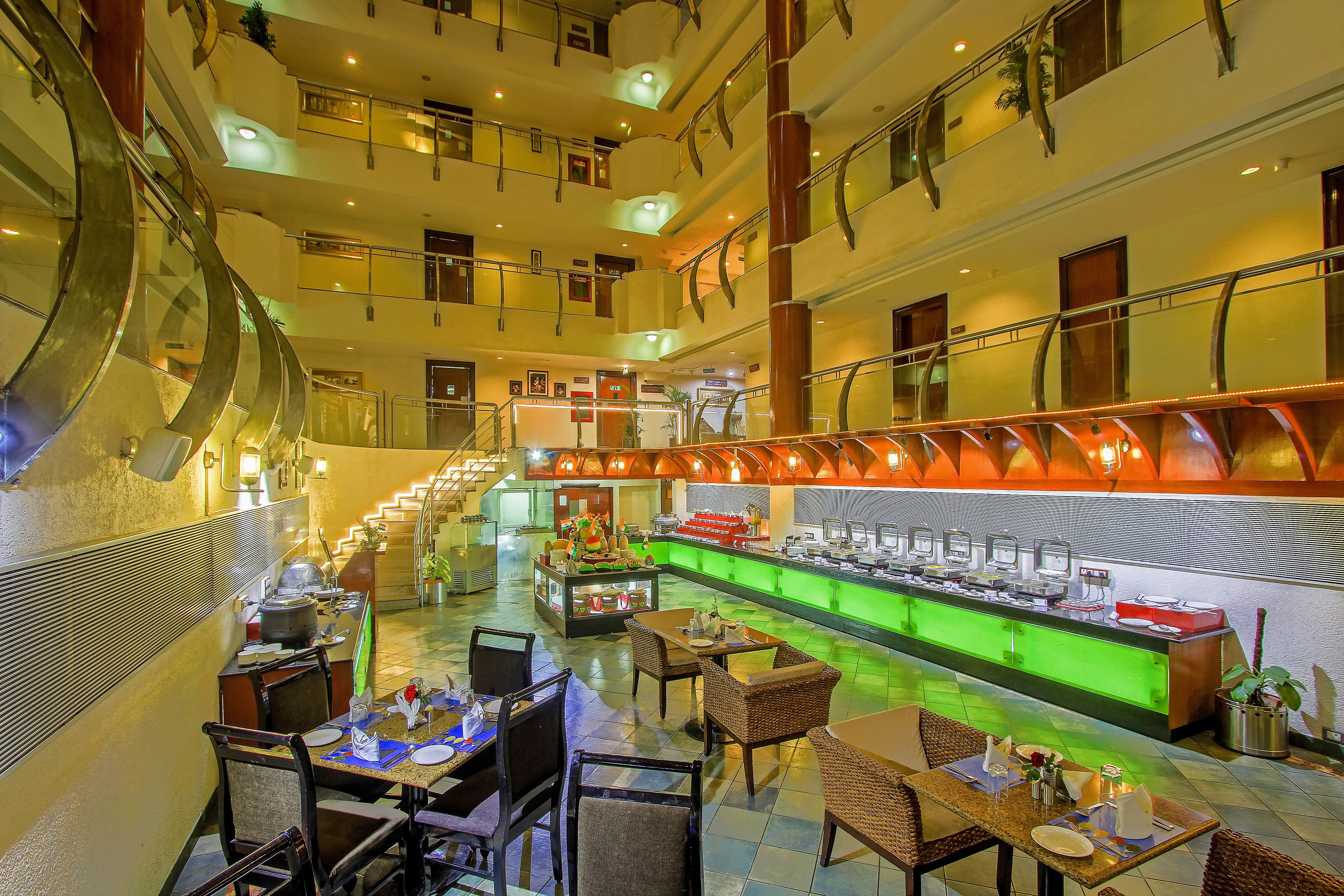 A multi-level hotel lobby with a central food bar, seating areas, and a staircase.