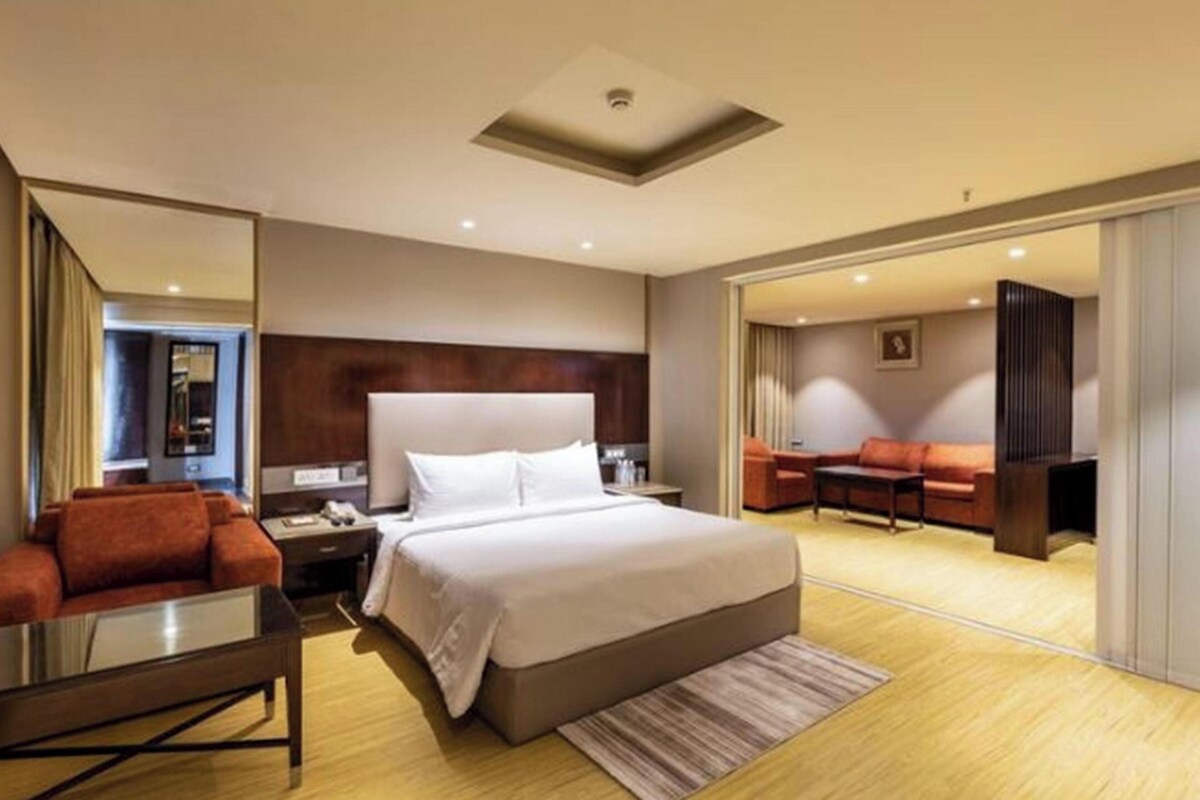 A hotel room with a large bed, a desk, a sofa, and a view of the city.