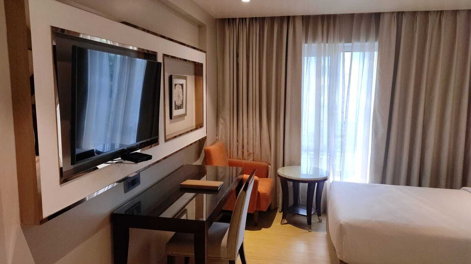 Et hotelværelse med seng, skrivebord med stol, fjernsyn og et lille bord.