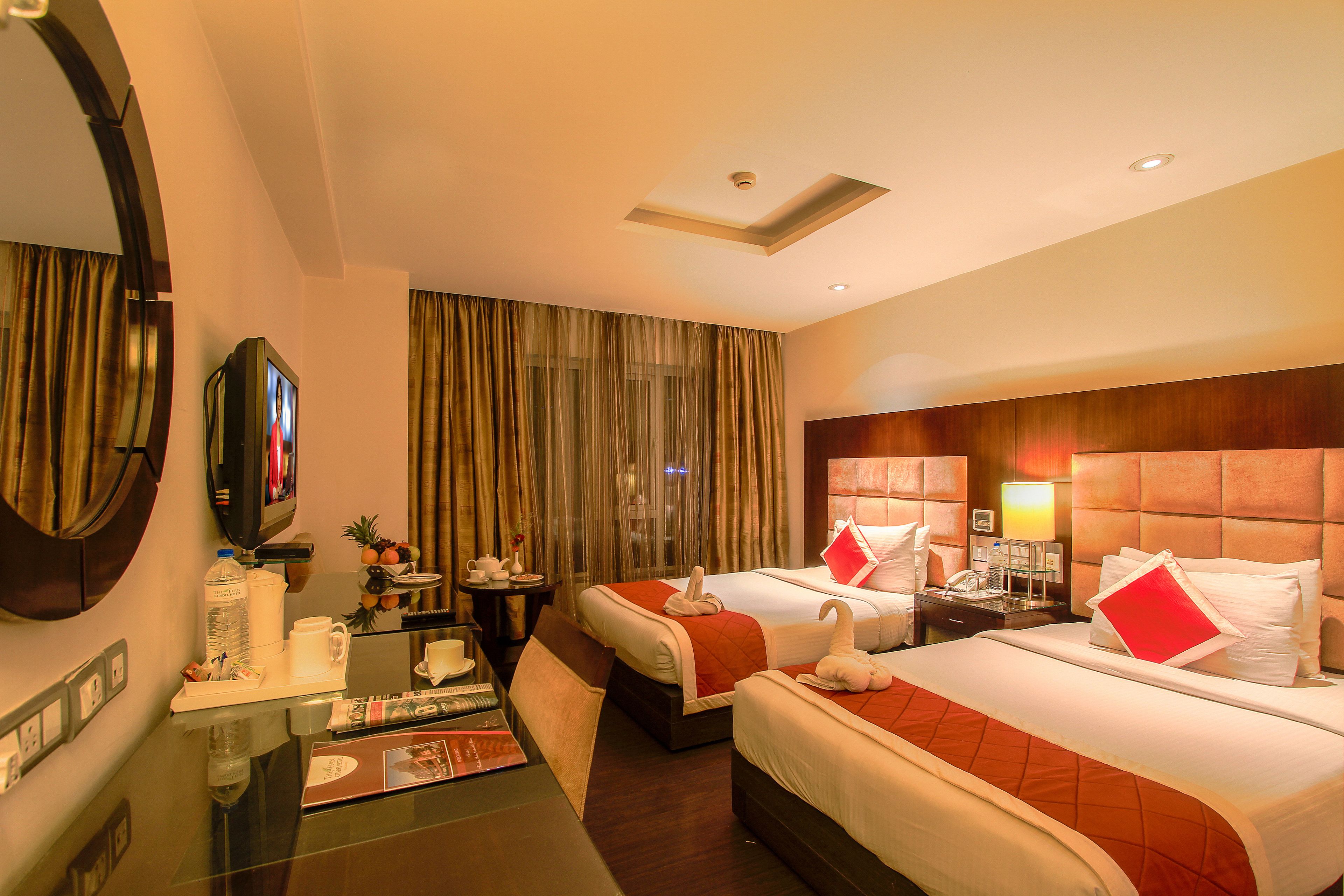 Ein Hotelzimmer mit zwei Betten, einem Schreibtisch mit Stuhl, einem Fernseher und einer Minibar.
