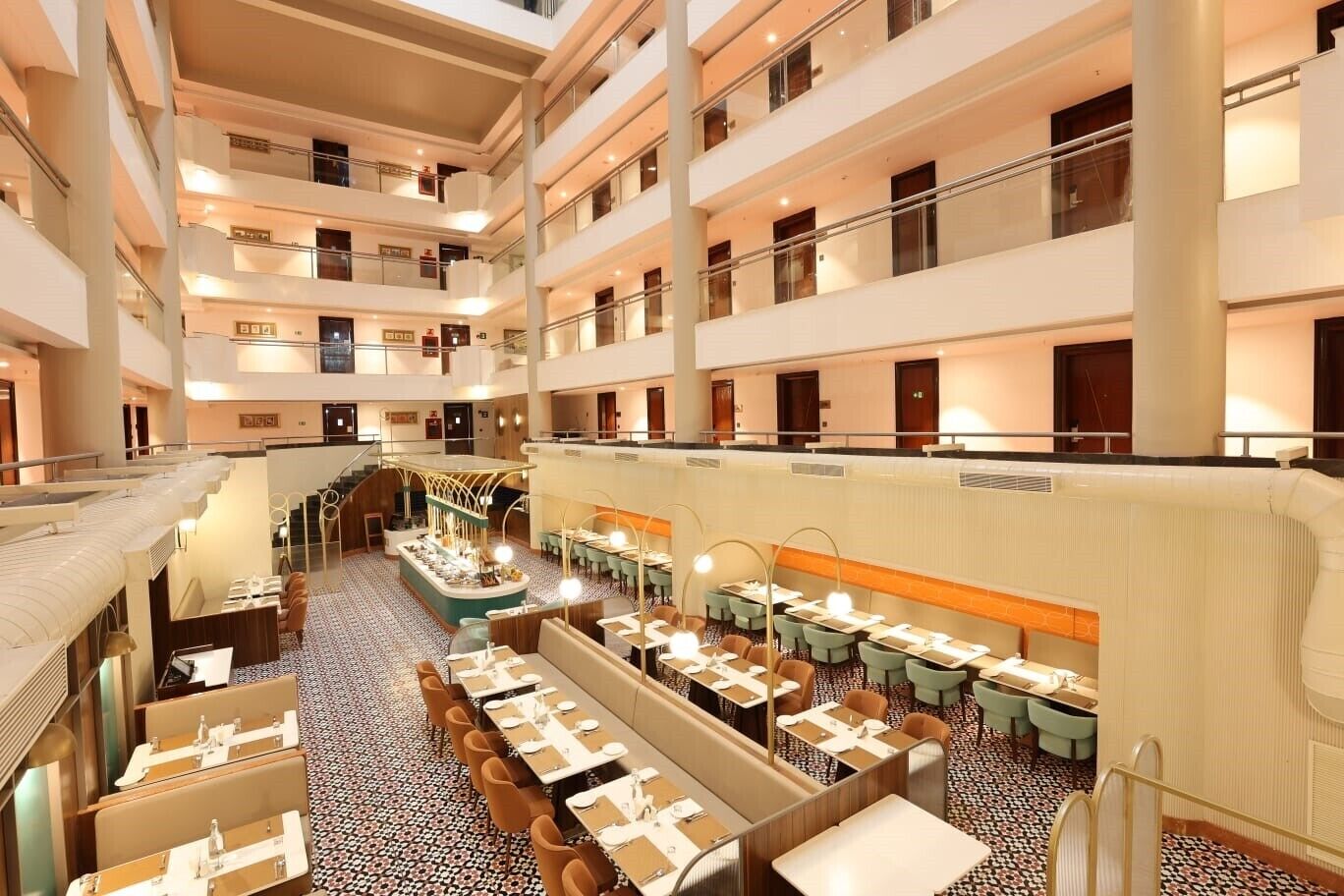 Un hall de hotel de varios niveles con un atrio central, varias zonas de restauración y una escalera que sube a los pisos superiores.