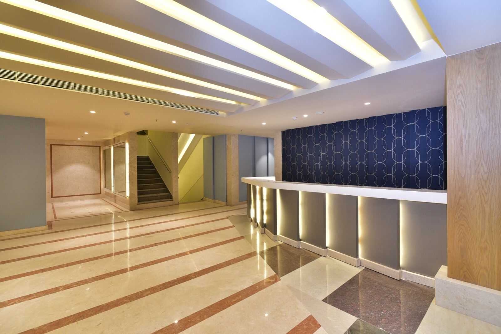 A spacious lobby with a polished marble floor, a staircase, and a reception area with a patterned wall.