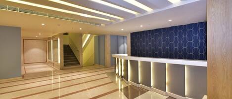 A spacious lobby with a polished marble floor, a staircase, and a reception area with a patterned wall.