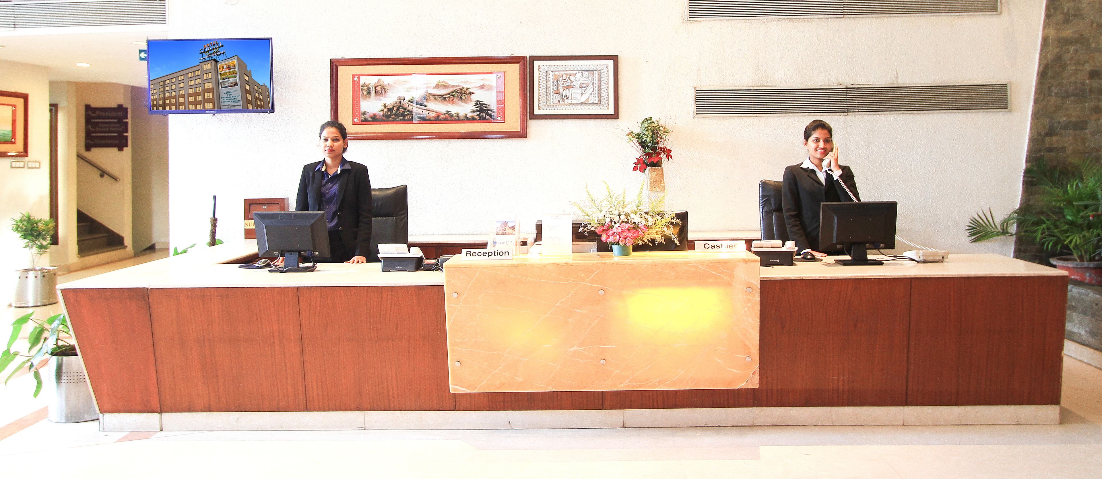 A reception desk with two receptionists, a computer, a phone, and a vase with flowers.