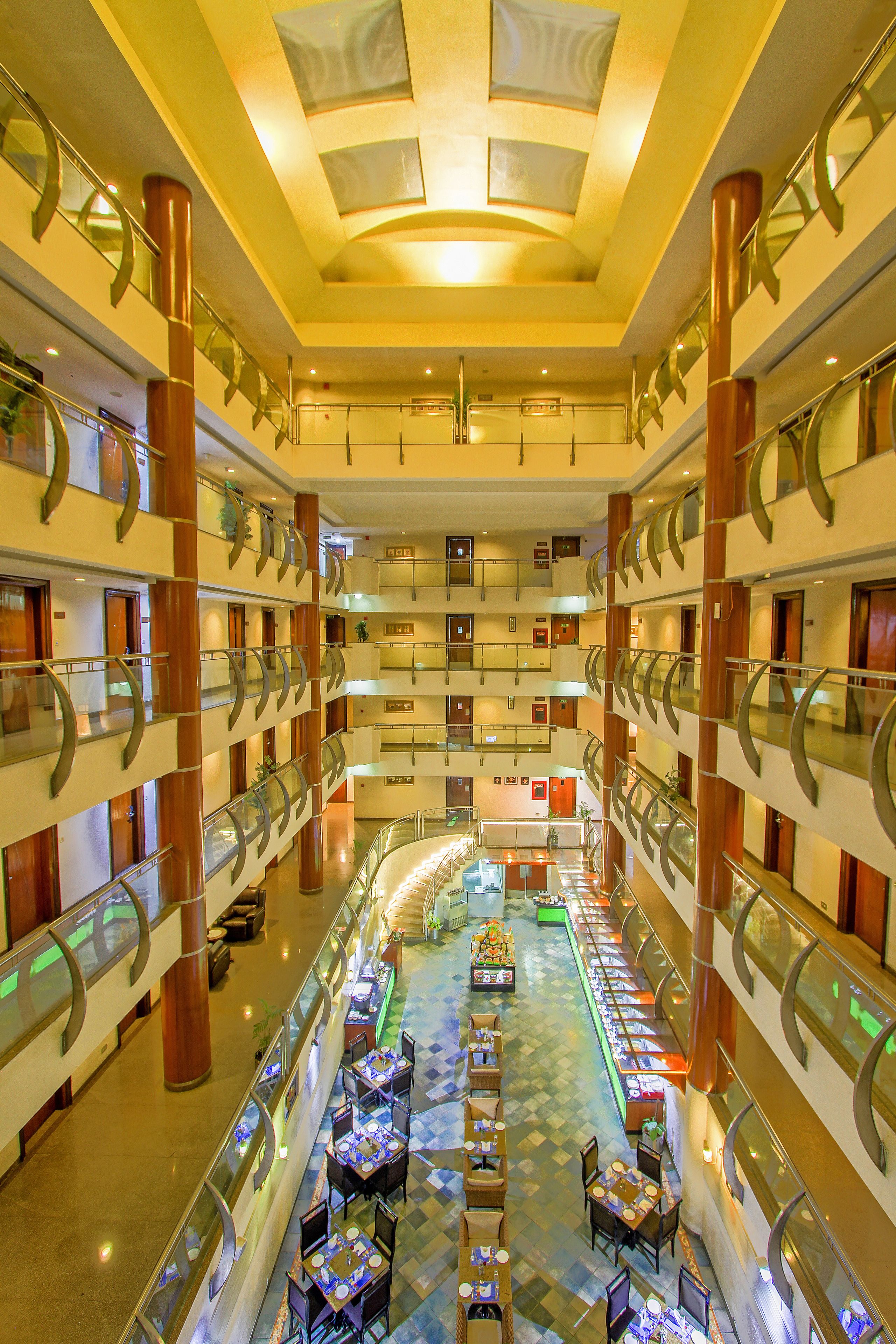 A multi-level hotel lobby with a central atrium, glass railings, and multiple dining areas.