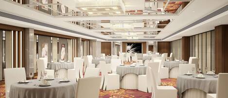 A banquet hall with multiple round tables, white chairs, and a high ceiling with decorative elements.