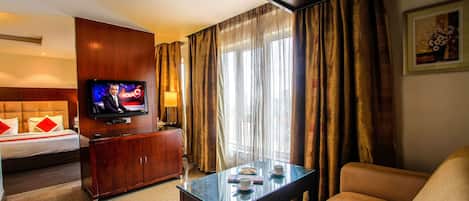A hotel room with a bed, a TV, a glass coffee table, a sofa, and a window with curtains.