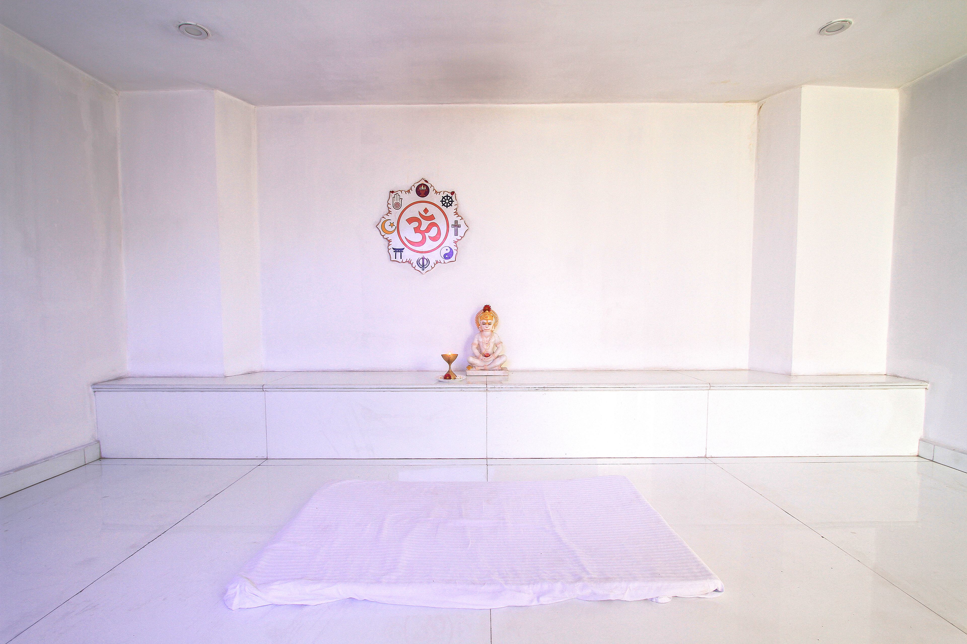 Una habitación limpia y vacía, con piso blanco, un banco y una estatua sobre una repisa.