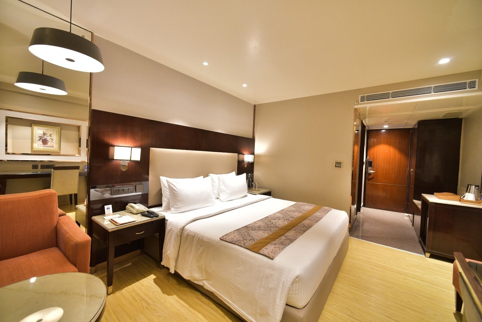 A hotel room with a bed, a desk, a chair, a bedside table, a lamp, and a wall-mounted TV.