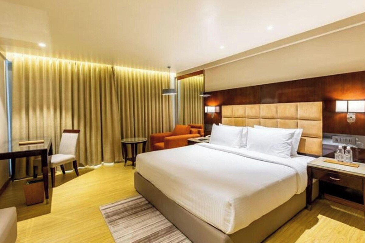 A hotel room with a large bed, a desk with a chair, a small table, and a sofa.