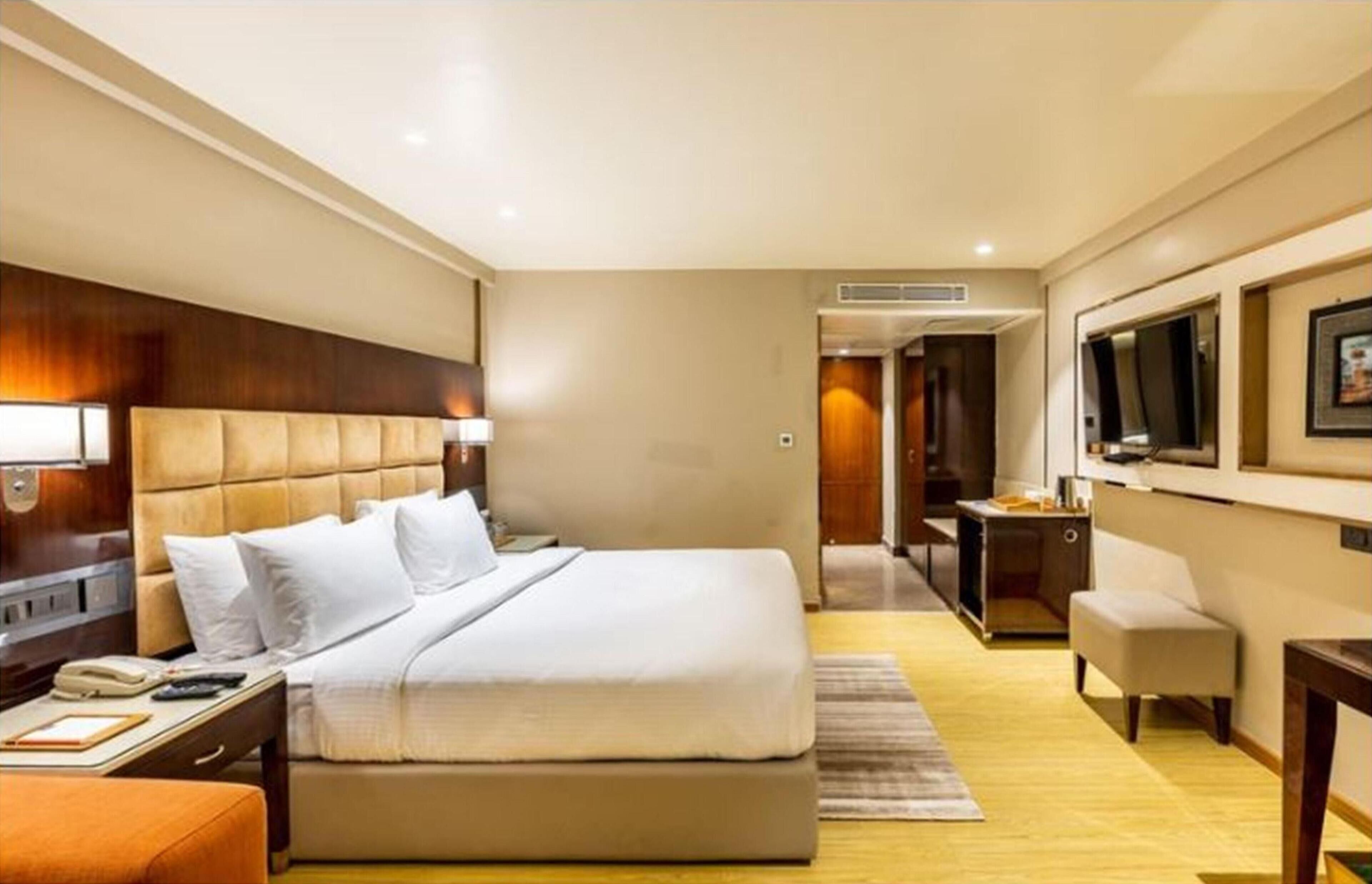 A hotel room with a large bed, a desk, a chair, a TV, and a bathroom.
