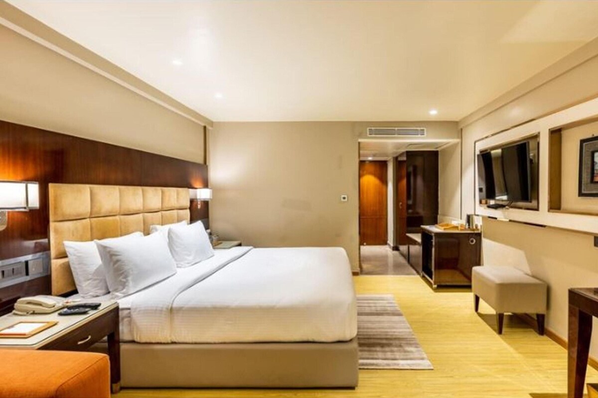 A hotel room with a large bed, a desk, a chair, a TV, and a bathroom.
