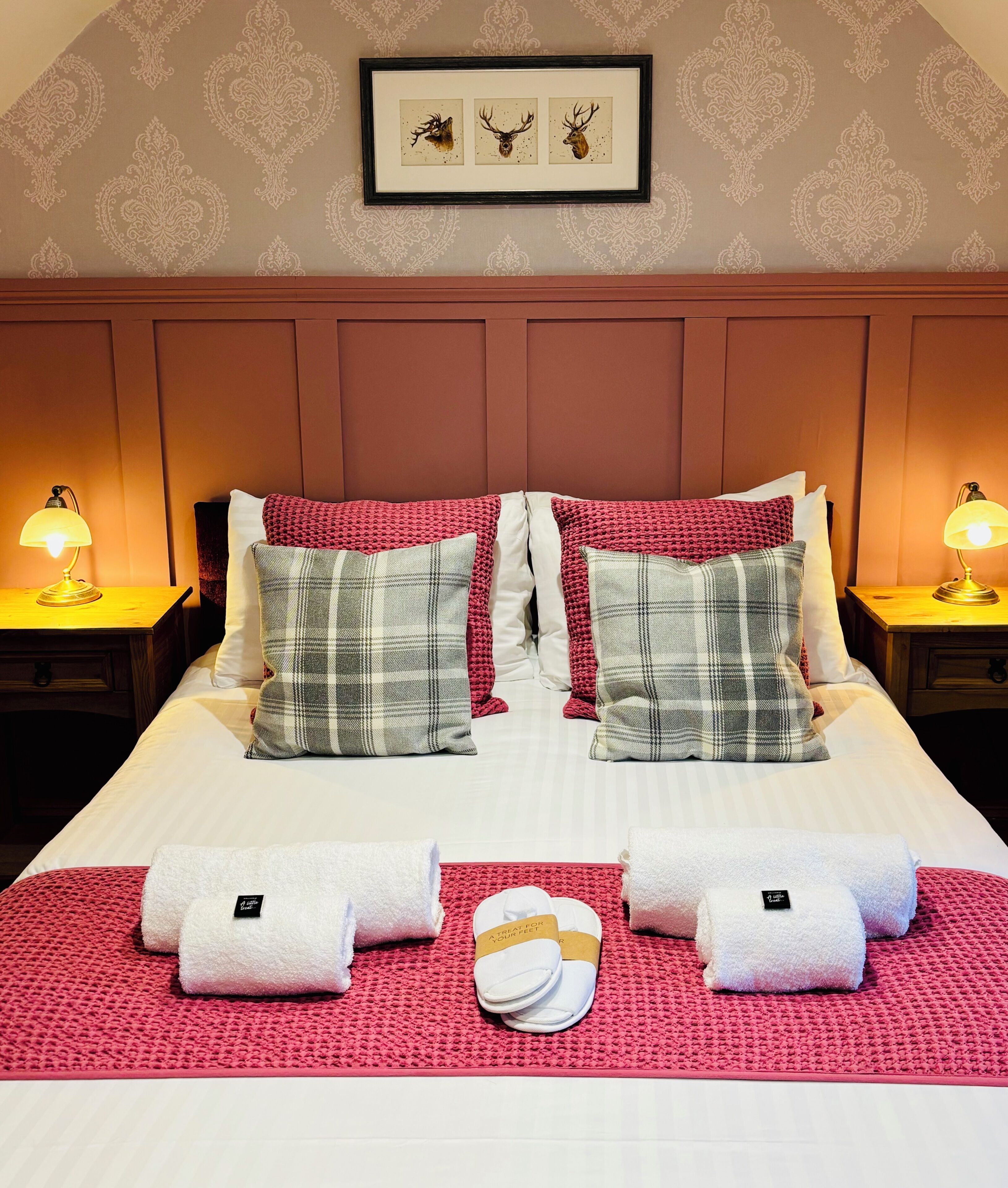 A neatly made bed with a red and white checkered blanket, two pillows, and two towels on a red mat.