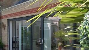 A modern building with large glass sliding doors, a brick facade, and potted plants outside.