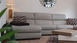 A modern living room with a grey sofa, a wooden coffee table, and a decorative mirror on the wall.