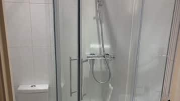 A glass-enclosed shower with a handheld showerhead and a wall-mounted faucet.