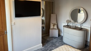 A modern bedroom with a flat-screen TV, a round mirror, a dresser, and a small ottoman.