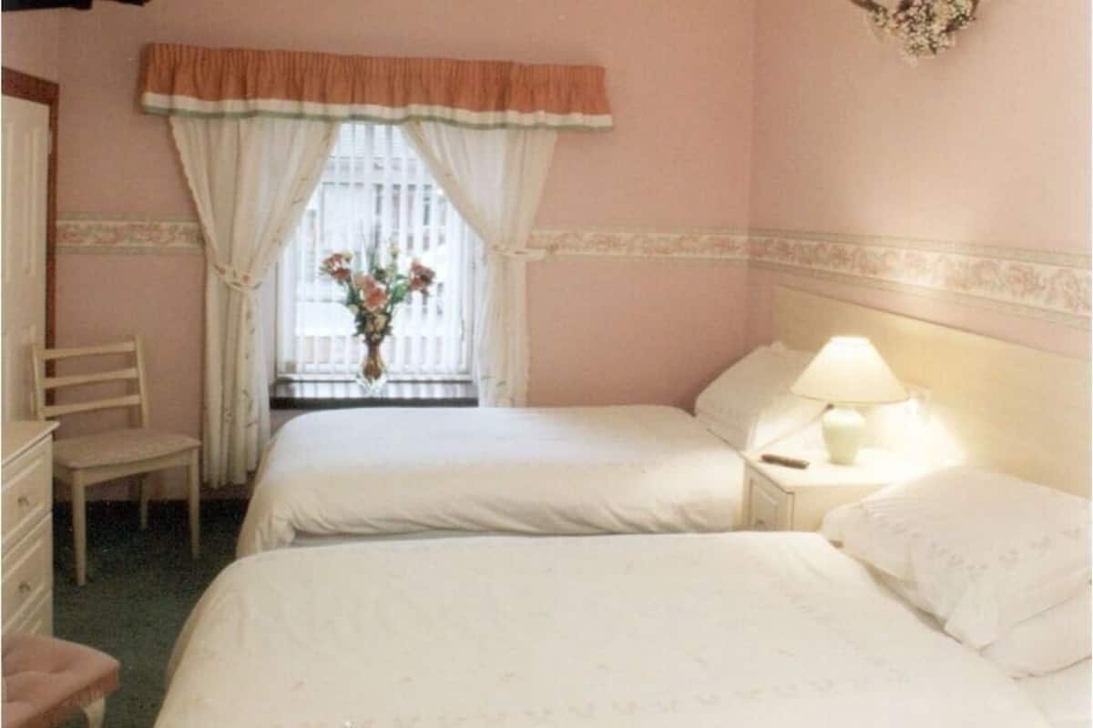 Una habitación con dos camas, una silla, un escritorio y una ventana con cortinas.