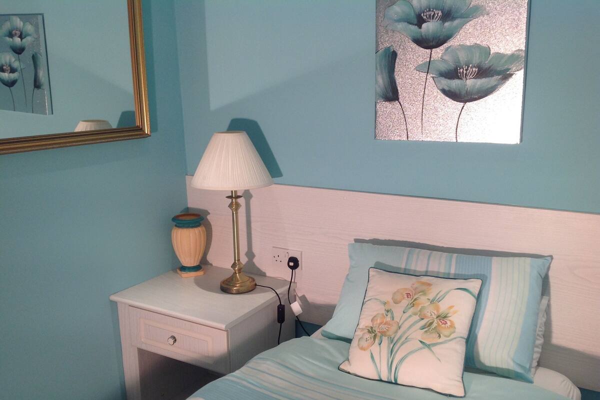 Un dormitorio con cama, mesita de noche, lámpara y un cuadro colgado en la pared.