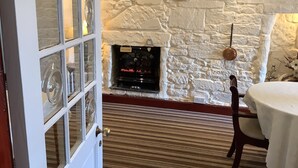 A room with a stone wall, a fireplace, a white door with glass panels, and a striped carpet. - Shawlee Cottage (Airdrie)