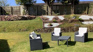 A patio with wicker furniture, a stone wall, and a wooden fence. - Shawlee Cottage (Airdrie)