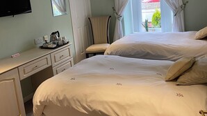 A bedroom with two beds, a desk with a flat-screen TV, a chair, and a window with curtains. - Shawlee Cottage (Airdrie)