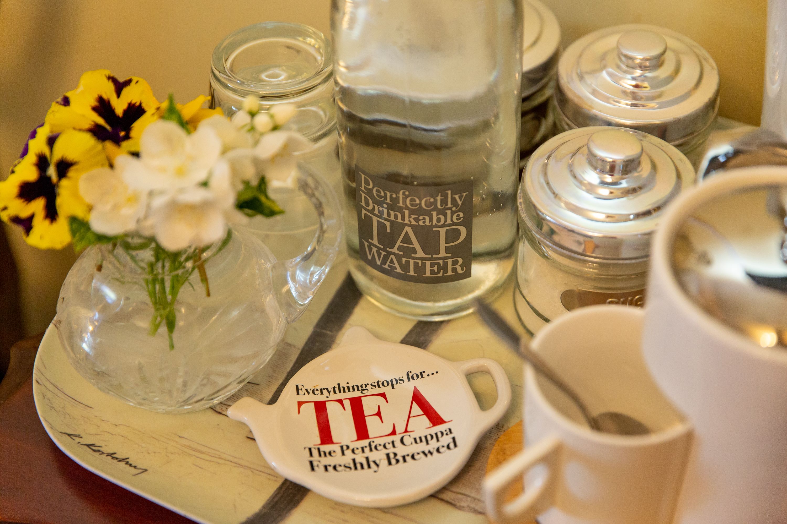 A tray with a water bottle, a tea cup, and a flower arrangement.
