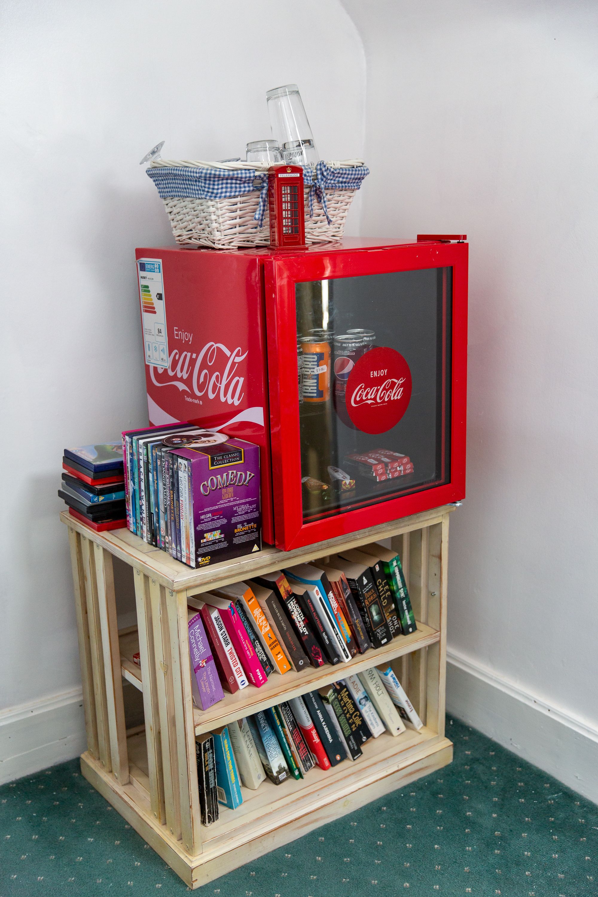Una pequeña estantería de madera con varios libros y un refrigerador rojo de Coca-Cola.