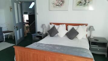 Un dormitorio con cama de madera, dos mesitas de noche, una mesita auxiliar, una silla y una puerta que da a otra habitación.
