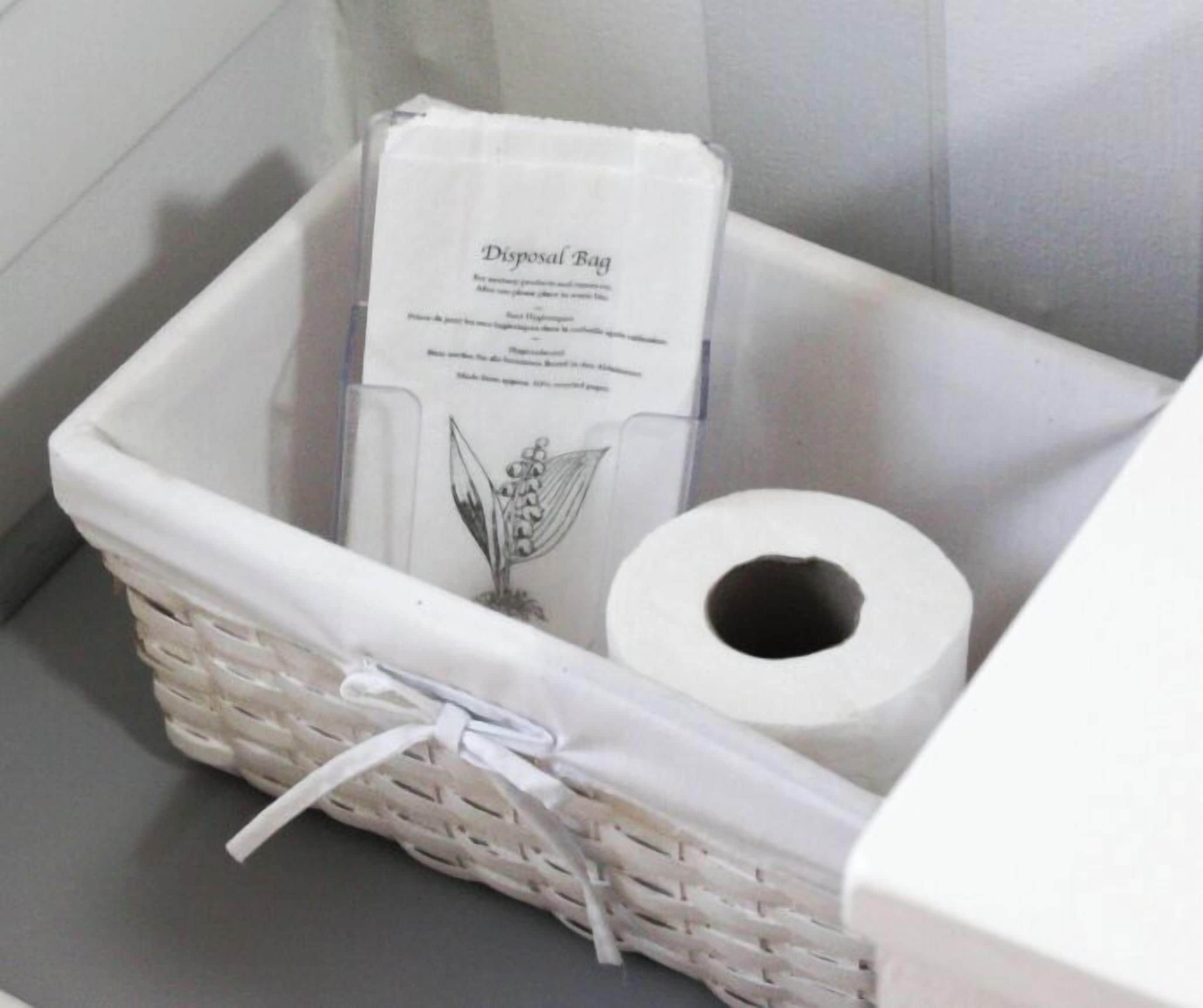 A white wicker basket containing a disposal bag and a roll of toilet paper.