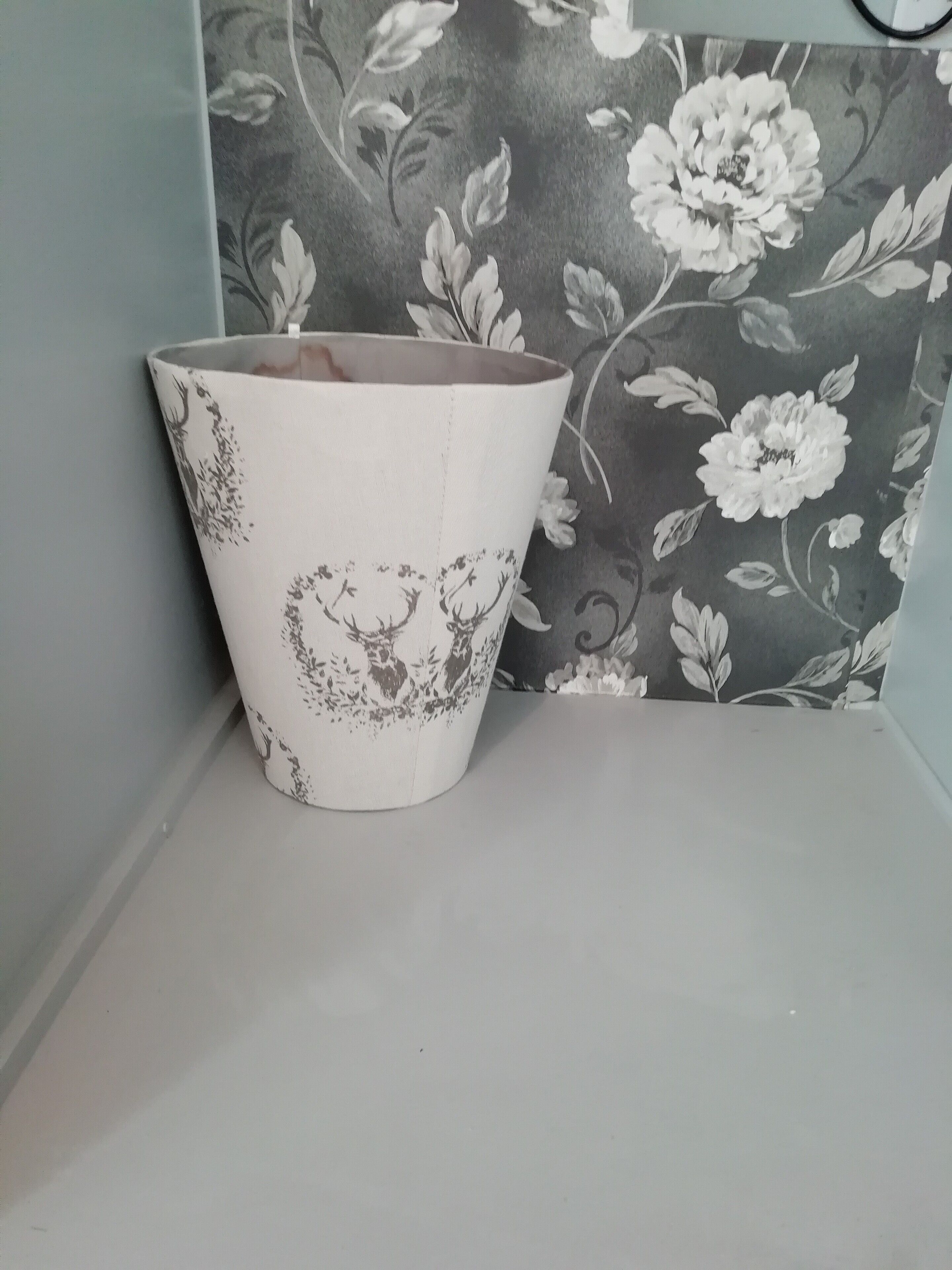 A white ceramic pot with floral designs on a shelf against a floral wallpaper background.