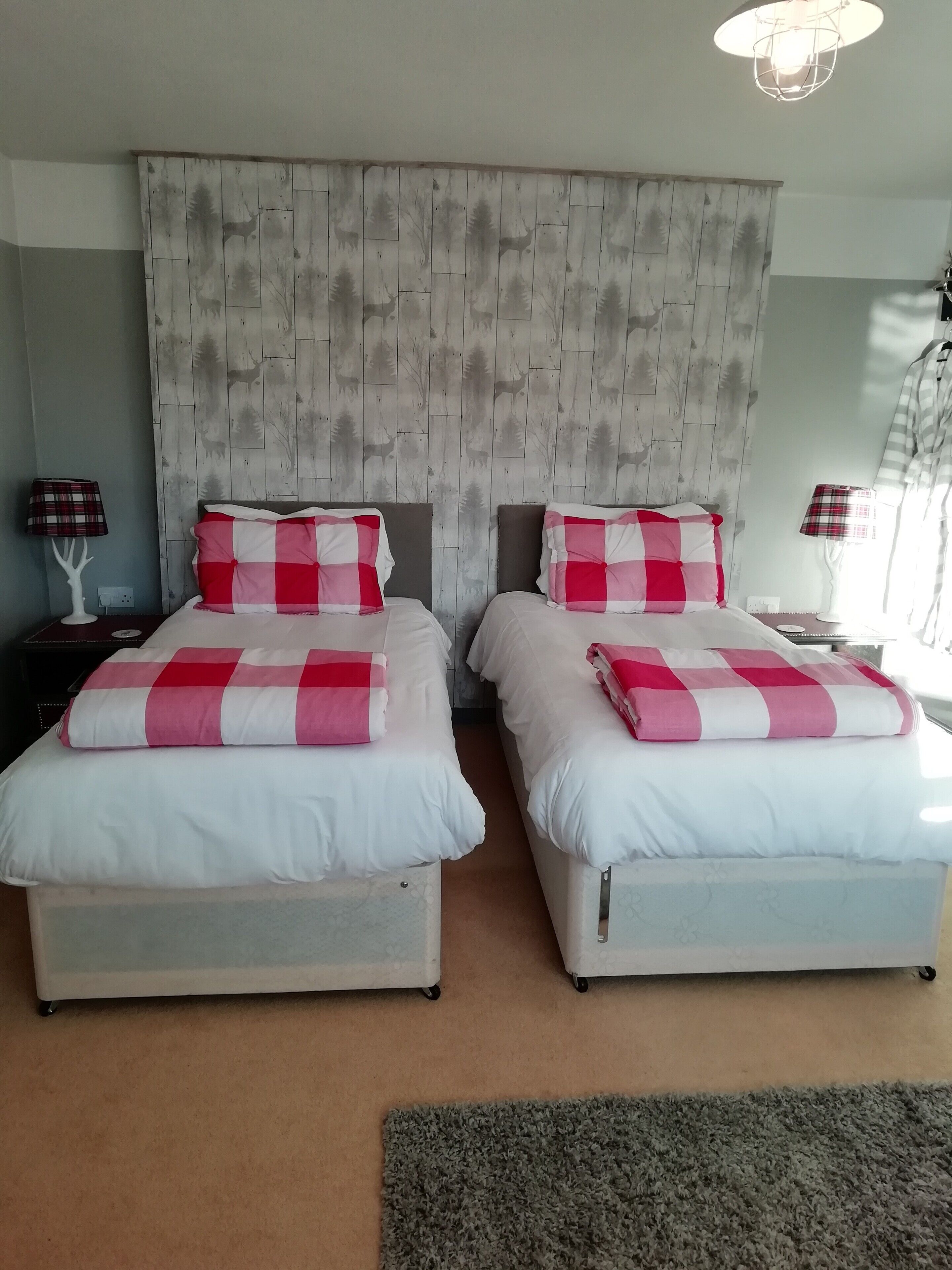 Habitación doble con dos camas, cada una con una manta a cuadros, un cabecero de madera y una mesita de noche con lámpara.