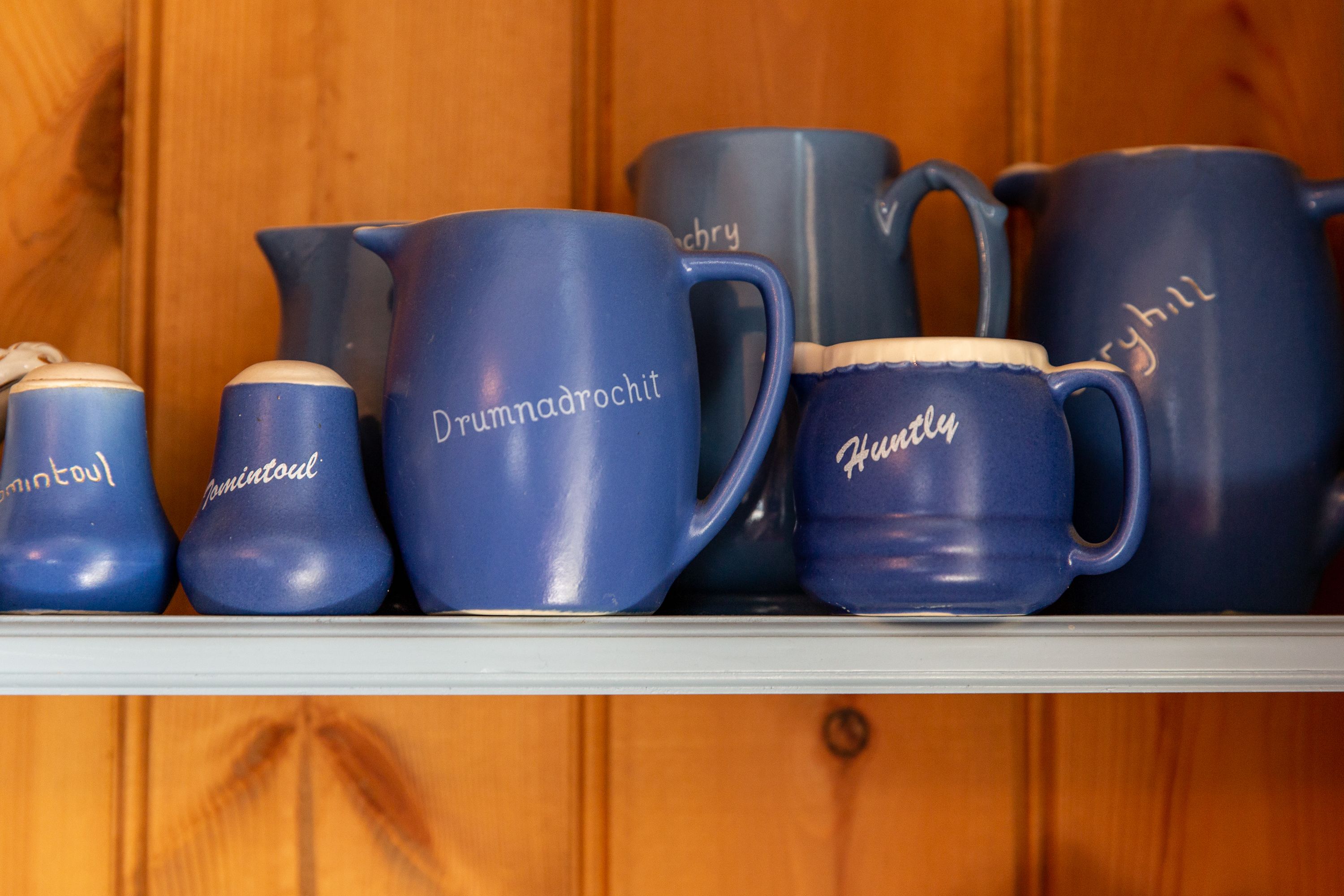 A shelf with various blue ceramic mugs and a pitcher, each with different text.