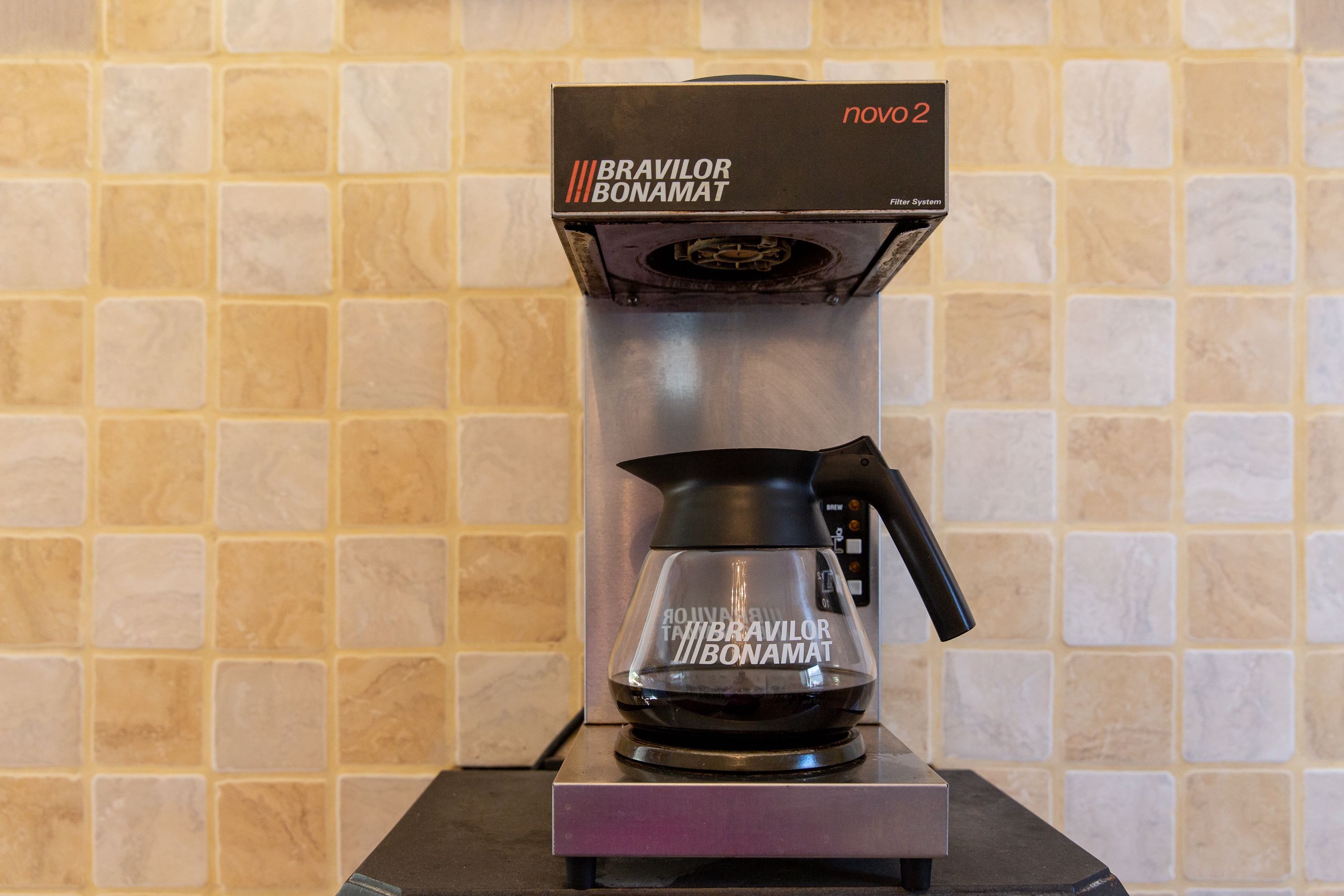 A coffee maker with a transparent water reservoir and a black drip tray, placed on a metallic stand.