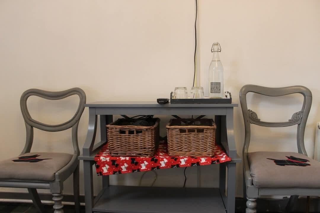 Una habitación con dos sillas, una mesa con cestas, una botella y un mantel rojo estampado.