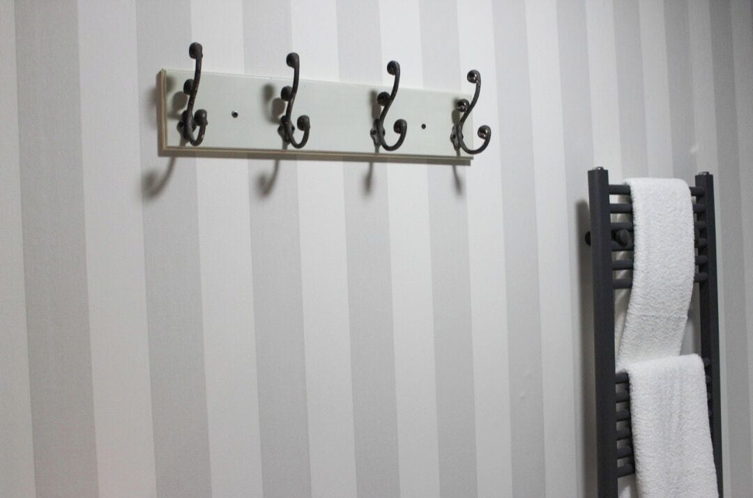 A bathroom with a striped wall, a towel rack with a white towel, and a towel rack with a black towel.