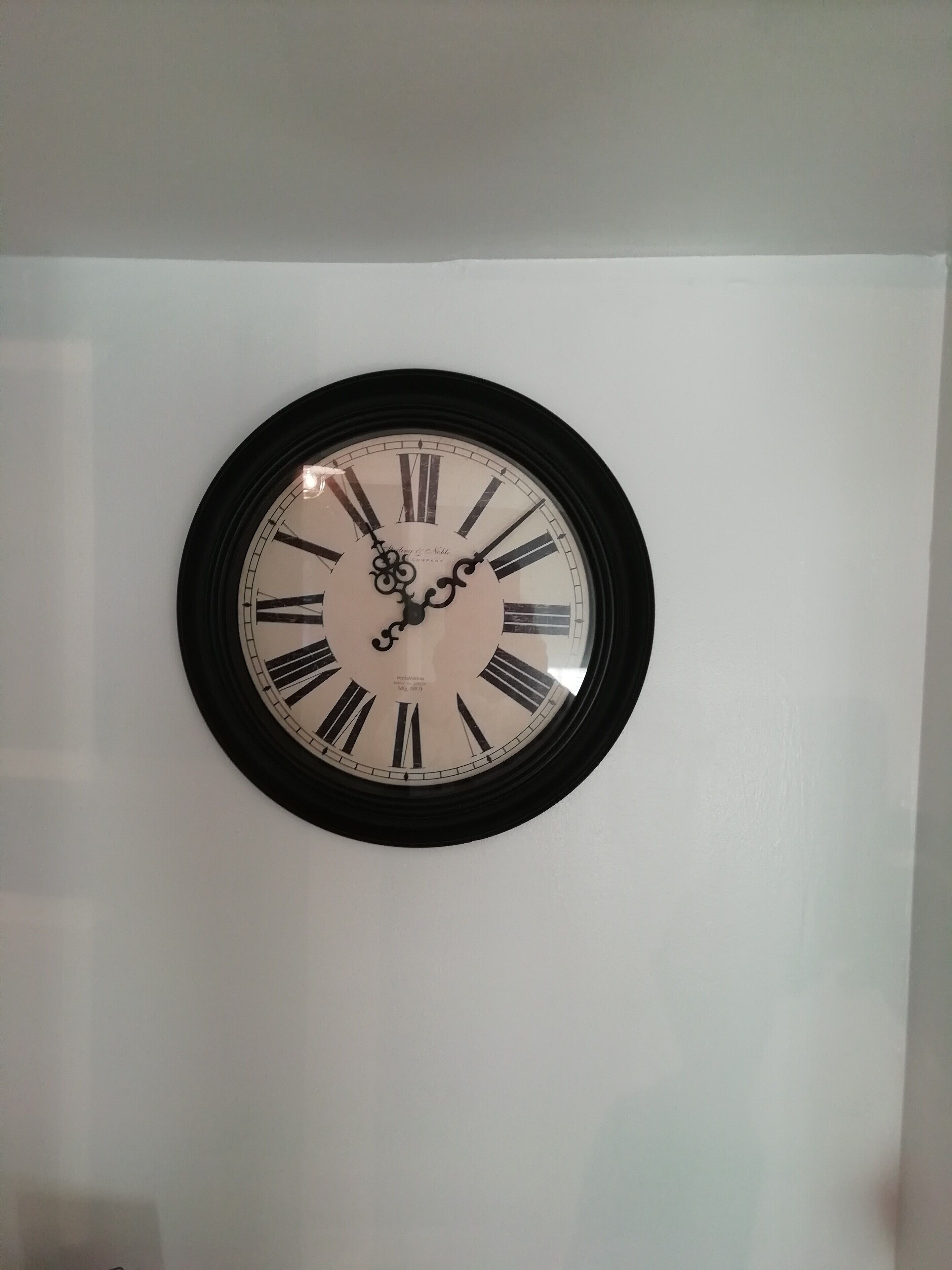 Une horloge murale ronde, avec des chiffres romains et un cadre noir.