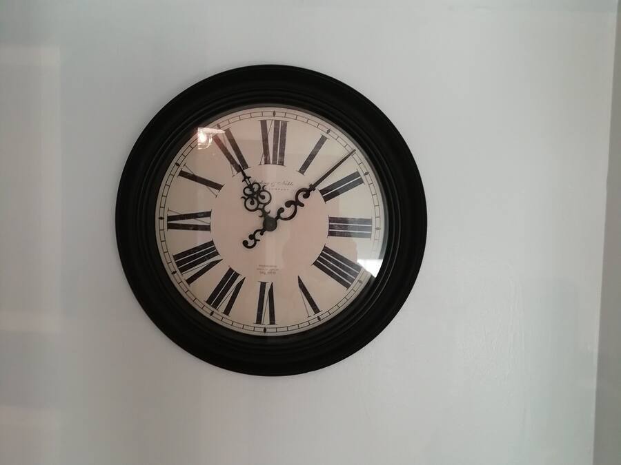 Une horloge murale ronde, avec des chiffres romains et un cadre noir.