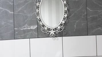 A bathroom with a white vanity, a marble backsplash, and a decorative mirror.