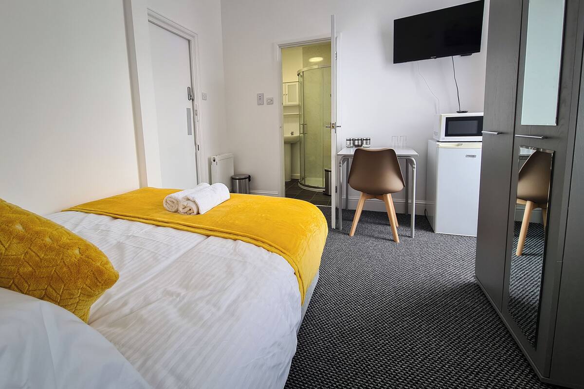 Et hotelværelse med seng, skrivebord, stol, tv og et lille tekøkken.