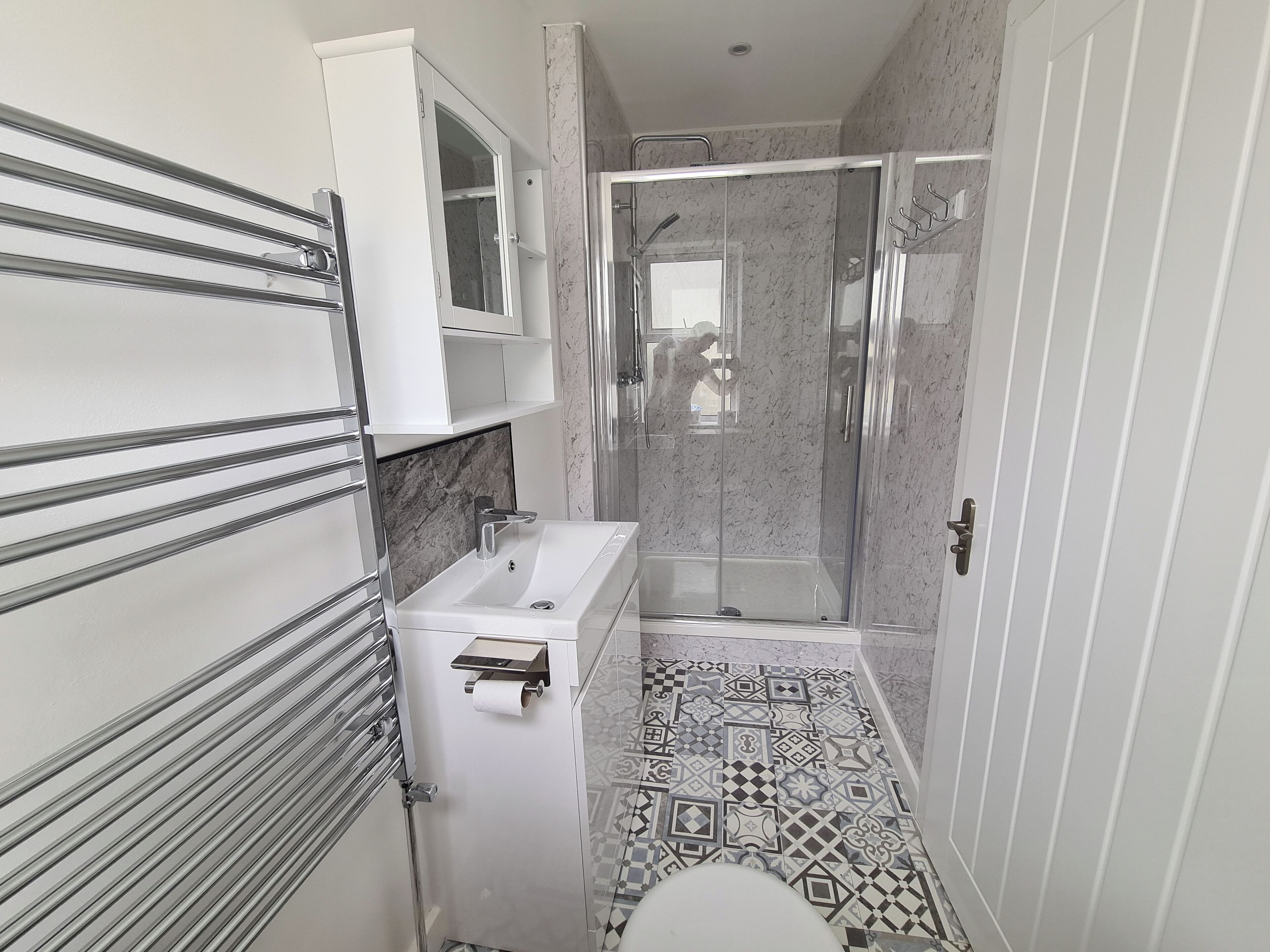 Un baño moderno con ducha envuelta en vidrio, un lavabo blanco y un suelo estampado.