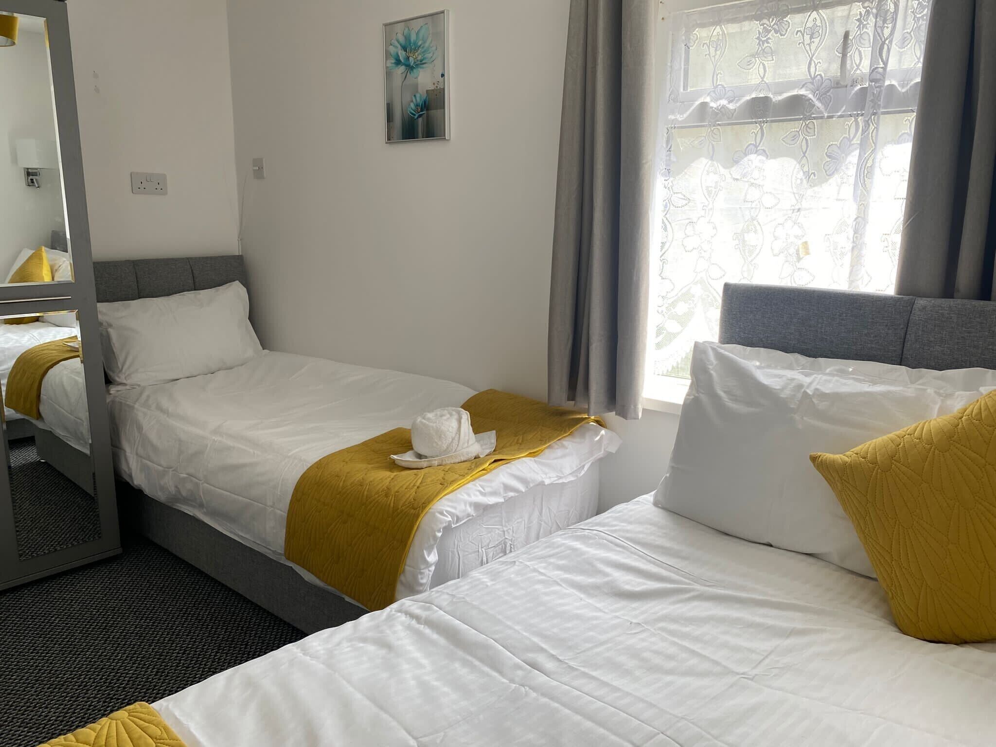 Habitación de hotel con dos camas, una ventana con cortinas, un pequeño cuadro en la pared y un espejo.