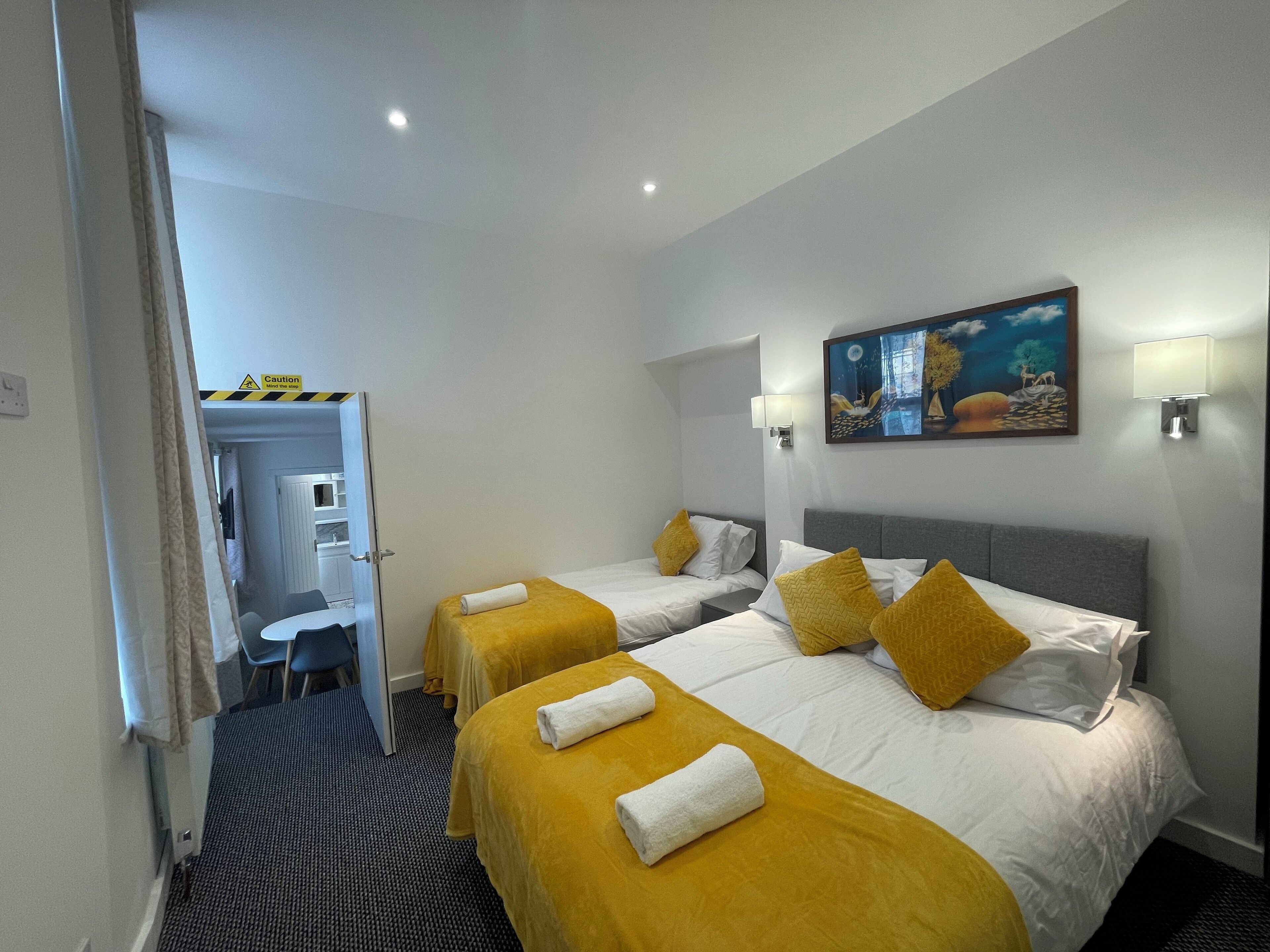 A hotel room with two beds, each with a yellow bedspread and white pillows, and a painting on the wall.