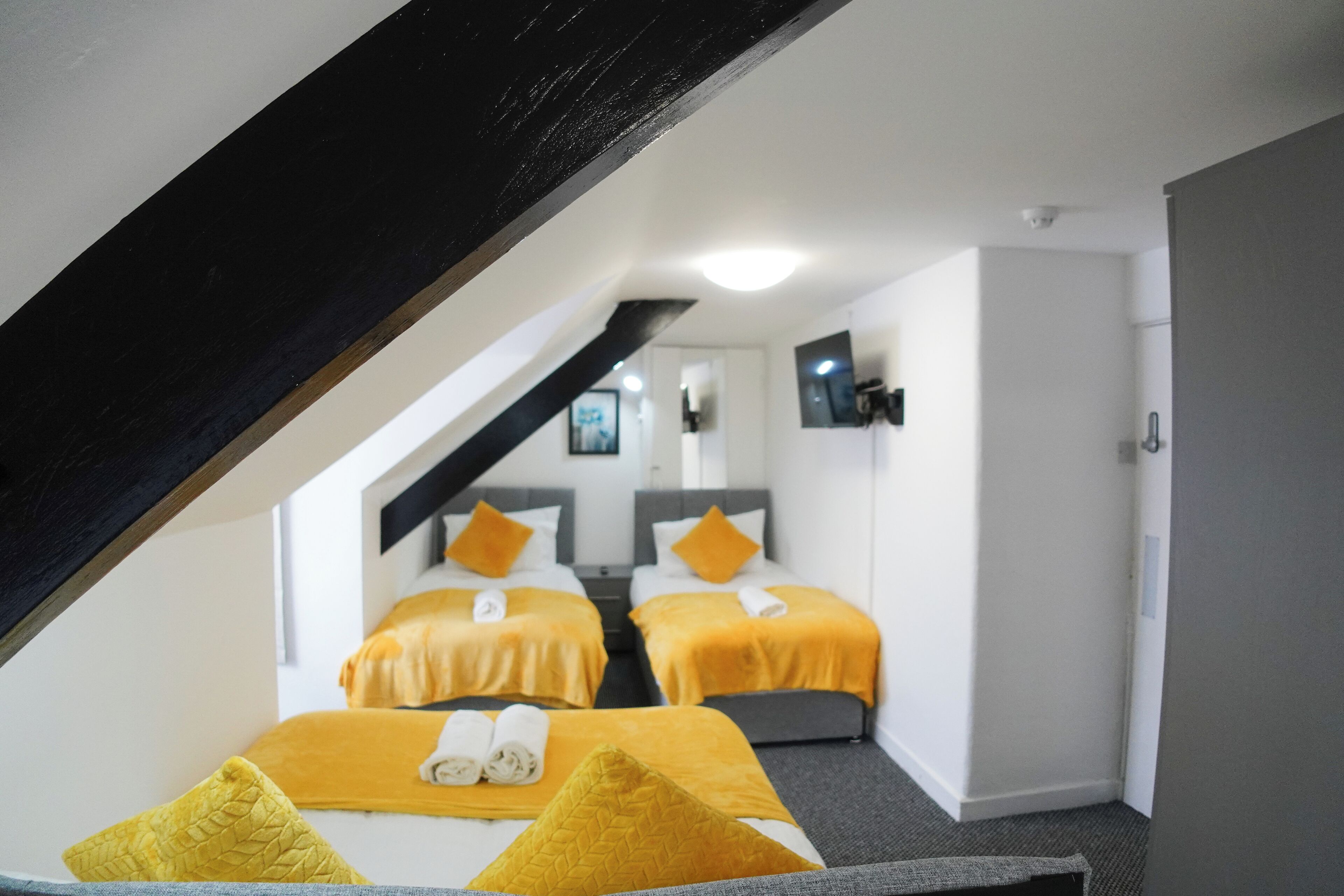 A hotel room with two beds, each with a yellow bedspread and matching pillows. There is a staircase leading to an upper level.