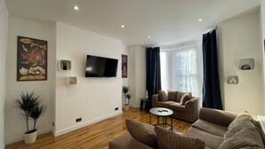 Uma sala de estar com televisão de tela plana, sofá, mesa de centro e um vaso com planta.