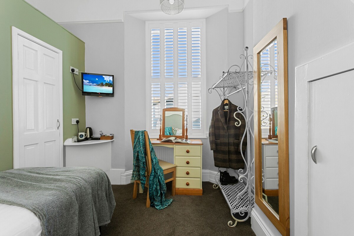 A bedroom with a bed, a desk with a chair, a TV, a window with shutters, and a wardrobe with a mirror.