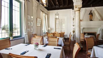 A restaurant with multiple dining tables, wicker chairs, and a fireplace.