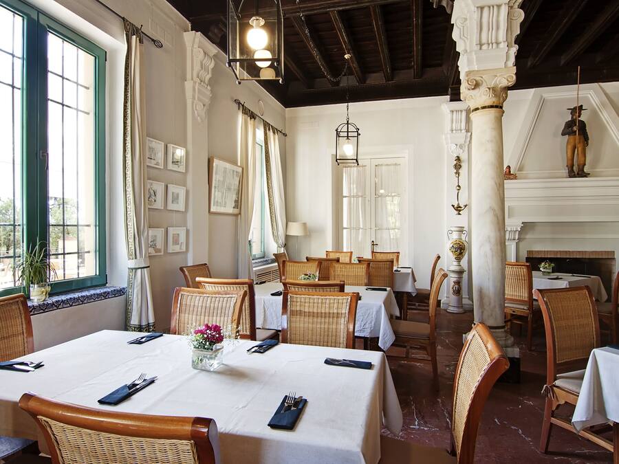 A restaurant with multiple dining tables, wicker chairs, and a fireplace.