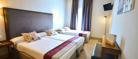 A hotel room with two beds, a desk, a chair, a TV, and a lamp.